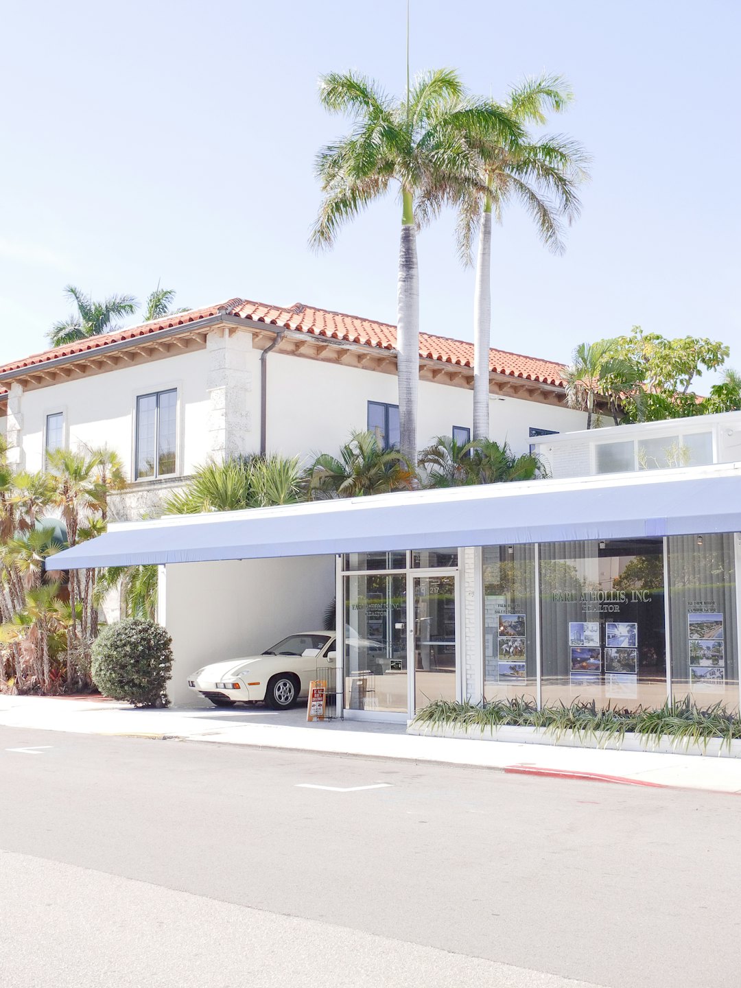White building with real estate office and vintage car parked outside.
