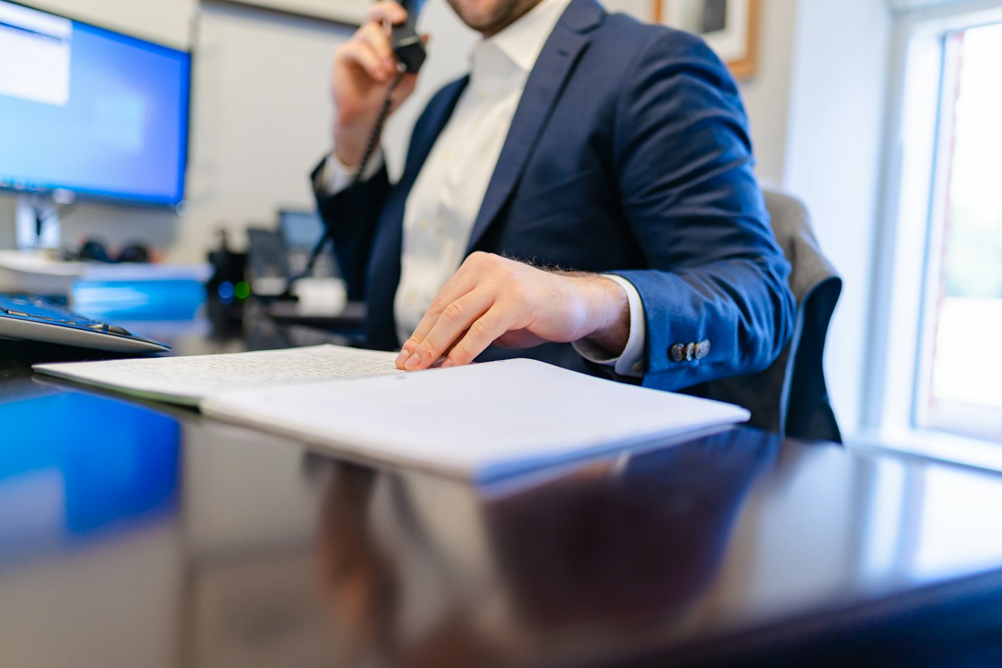 Businessman in a suit talking on a landline phone at his desk.